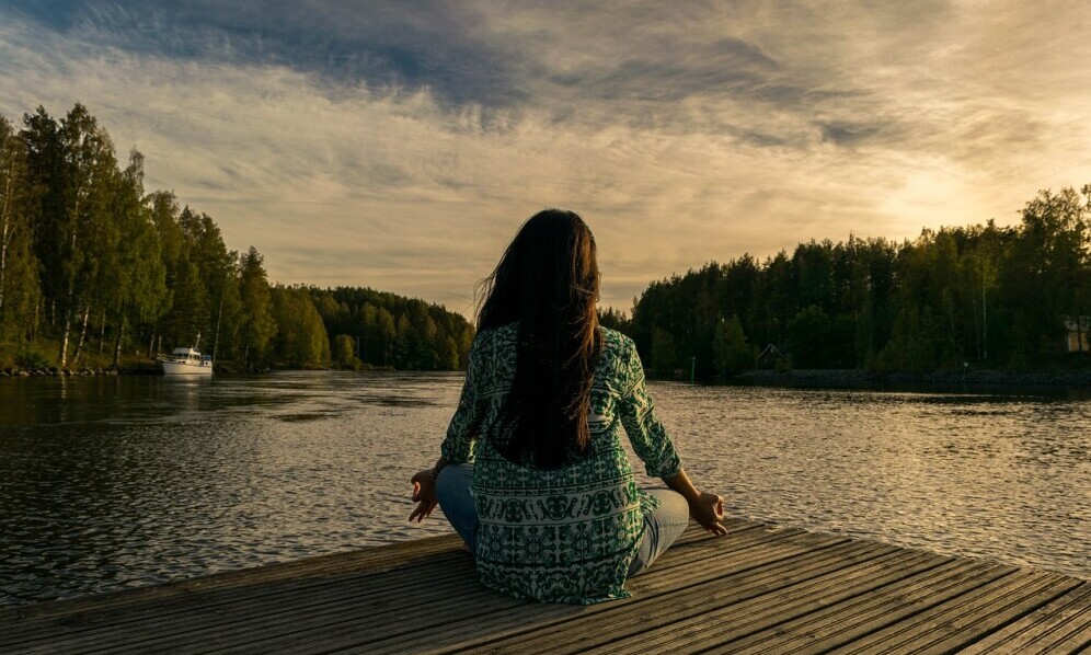 girl sitting peacefully by a lake meditating