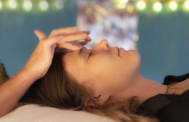 A woman lying on a therapist's couch receiving Reiki treatment