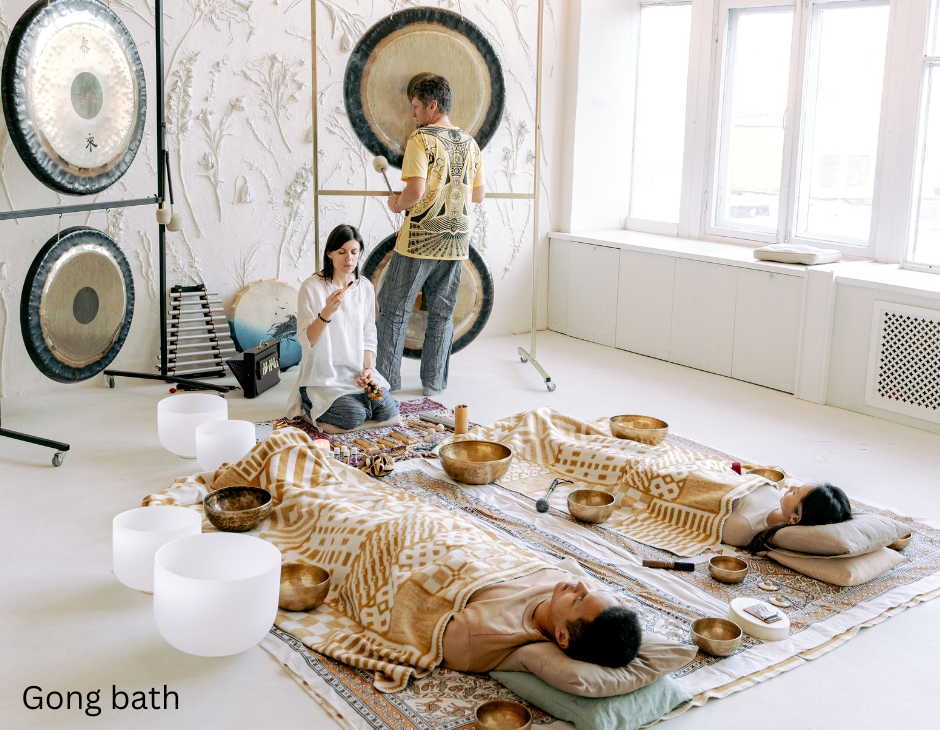 Two people lying on the ground covered by blankets as two other people play gongs to show Sound Healing for Beginners